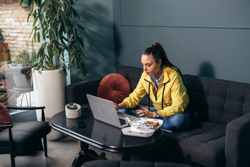 woman at home using laptop and havinsg lunch or snack