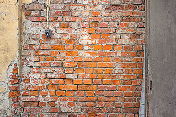 Red yellow gray wall background. Old damaged red brick wall with yellow plaster. Switch on the wall. Brushed metal door in the brick wall. 