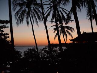Sunset, silhouette of palm trees. Travel concept, palm trees on the background of the sea at sunset time. Sunset on the ocean coast, mountains, sea, beach, sky, clouds Bali, Indonesia.