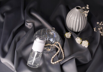 Luxury cosmetics concept. Still life on a shiny, delicate gray fabric. Beauty product with vase, flowers and glass form, pearl beads and hairpins with roses