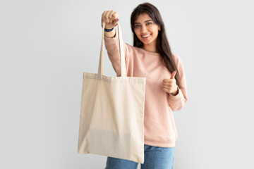 Cheerful woman standing with blank canvas tote bag
