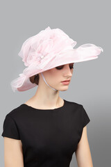 Romantic lady is wearing pale pink hat for evening party. Organza hat with chin strap is decorated...