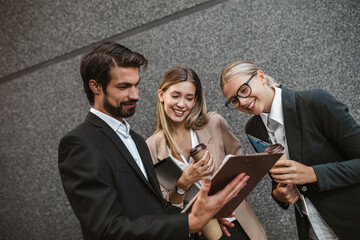 Office colleagues talking outdoors near the office building, discussing new project, holding clipboard and digital tablet.