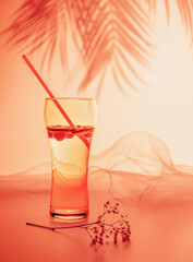 Blurred composition with glass of natural fizzy lemonade with a straw on pink background of the sunset with palm shadows. The concept of no alcohol tropical holiday resort and relax and summer party