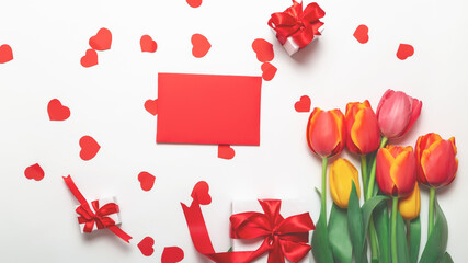 A bouquet of fresh tulips with envelope and a gift box with a red ribbon on a white background. Top view. Flat composition. Women lifestyle and holidays concept