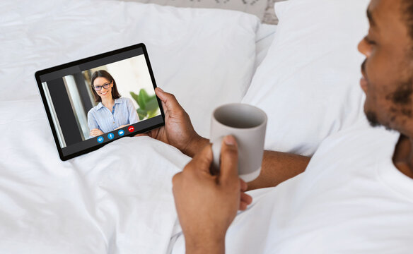 Young African Man Relaxing In Bed With Digital Tablet, Making Video Call