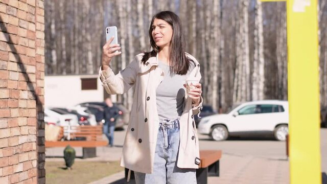 A happy brunette girl takes a video of herself on a smartphone
 while walking along a city street.Slow motion.