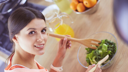 Smiling young woman mixing fresh salad in the kitchen.