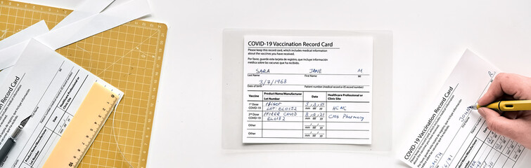 Banner, Fake covid vaccination record card. Covid scams. Forged health certificate with false vaccination record against covid. Blank card, pen, paper knife,laminator. Flat lay on white with yellow.