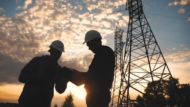 silhouette of an electricians engineers working next to an electrical support tower energy. electricity high teamwork tower support. electricals engineers inspect teamwork electricity sunset pylon