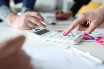 Businesswoman with pink manicure counting on calculator at meeting closeup