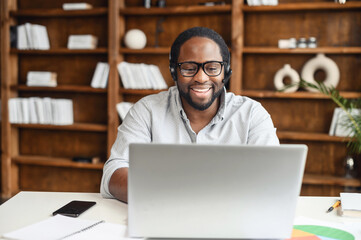 A multiracial guy using a hands free device for online communication sitting at the desk in modern office space, an African-American wearing headset holding video conference, webinar