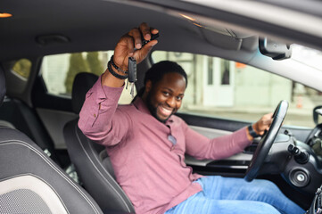 Selective focus at the car keys in hand of happy African-American man. Cheerful black guy buying a...