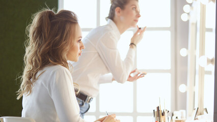 Fototapeta premium Make-up artist applying white eyeshadow in the corner of model's eye and holding a shell with eyeshadow on background