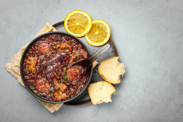 Feijoada in black bowl gray concrete table top. Brazilian and portuguese cuisines traditional beans meat stew