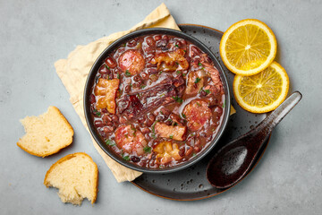 Feijoada in black bowl gray concrete table top. Brazilian and portuguese cuisines traditional beans meat stew