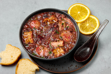 Feijoada in black bowl gray concrete table top. Brazilian and portuguese cuisines traditional beans meat stew