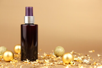 Obraz na płótnie Canvas Unbranded dark brown spray bottle, gold Christmas balls and pieces of gold paper on golden background. Cosmetic packaging mockup with copy space, front view. Body mist.