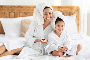 Beautiful mother and kid wearing bathrobes, showing pastry