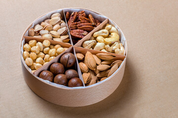 wooden round eco friendly gift box with triangular cells and mix of different types of nuts for a healthy diet of vegetarians on craft paper rustic background, nobody.