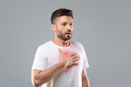 Man with chest pain touching inflammated zone, grey background