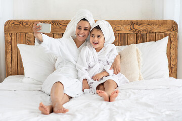 Obraz na płótnie Canvas Beautiful mother and daughter in bathrobes taking selfie on smartphone