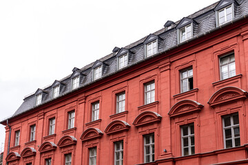 Fototapeta na wymiar Vibrant red stone tenement or apartment building with shiny black roof tiles, attic windows (dormers), many windows with geometric ornament and triangle pediments.