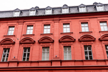 Vibrant red stone tenement or apartment building with shiny black roof tiles, attic windows (dormers), many windows with geometric ornament and triangle pediments.