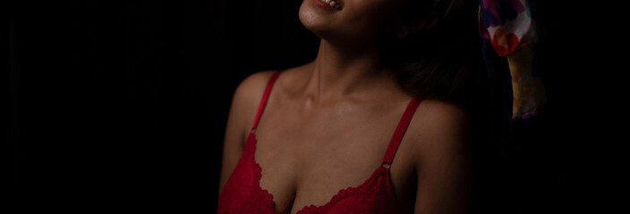 Portrait of an young and attractive Bengali Indian brunette girl wearing red lingerie posing in front of a black studio background. Indian lifestyle and boudoir photography.