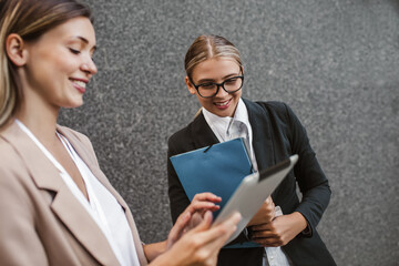 Caucasian woman assistant showing something on tablet device to businesswoman, talking and discussing work.