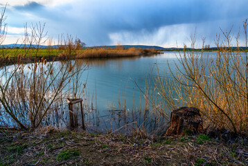 Lake shore in sunset and rain over horizon.