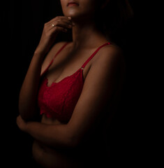 Portrait of an young and attractive Bengali Indian brunette girl wearing red lingerie posing in front of a black studio background. Indian lifestyle and boudoir photography.