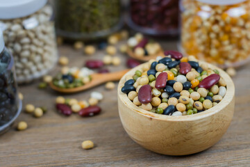 Various grains such as soybeans, black beans, red beans, dried corn in a wooden cup on a wooden table background.