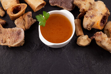 Bone broth on a stone surface next to boiled beef bones. Selective focus, copy space