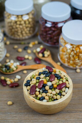 Various grains such as soybeans, black beans, red beans, dried corn in a wooden cup on a wooden table background.
