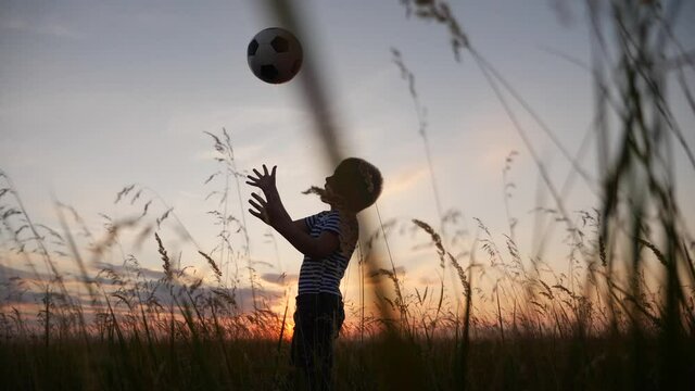 Childhood dream. boy play soccer ball in the park silhouette. fun happy family kid dream concept. kid boy play on the field silhouette at sunset carries a soccer ball. baby winner