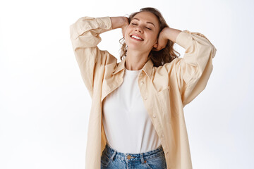 Carefree blond woman relaxing, touching hair and feeling free and happy, close eyes, enjoying leisure, standing against white background