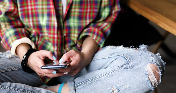 Anonymous casual woman sitting and holding in hands smartphone, typing text message via cellphone, charting in mobile phone, using modern device at home, lifestyle and communication concept.