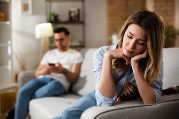 Couple at home after having a fight. Sad depressed woman sitting on sofa.