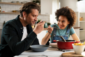 Boyfriend and girlfriend eating lunch together at home. Husband and wife enjoying in delicious food.