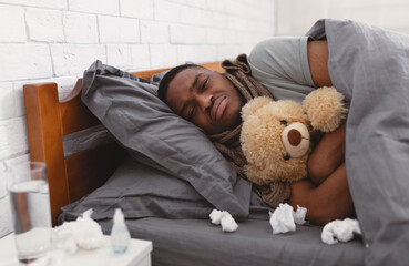 Depressed Sick African Man Hugging Teddy Bear Lying In Bedroom