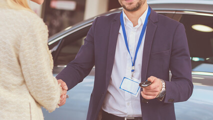 Car salesman sells a car to happy customer in car dealership and hands over the keys.
