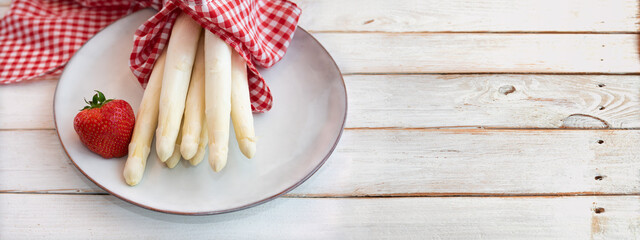 Uncooked white asparagus with strawbeery and red checkered cloth on vintage wooden planks. Fresh...