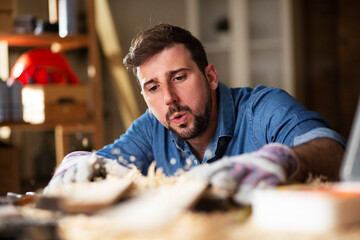 Young male carpenter working in workshop. Carpenter working on wood craft at workshop.