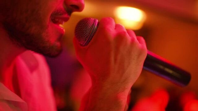 a bearded male singer sings into a microphone at karaoke or in a nightclub.
