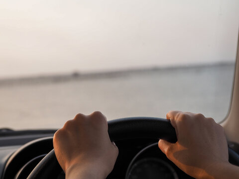 Two Hands Of The Woman Holding The Steering Wheel In The Evening, The Sun Shone Through The Glass.