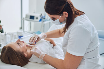 Obraz na płótnie Canvas Professional cosmetologist making anti aging biorevitalization for female client in cosmetic salon