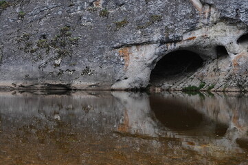 travel photography, rock formation with cave reflected in river waters front view. Selected focus