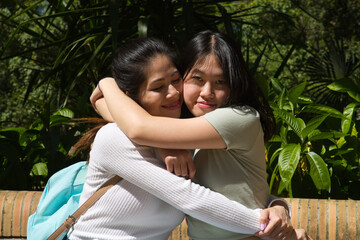 Two Asian women on holiday. They are sitting in a park and are hugging each other tightly. On their legs is a tourist map of the city. In her hand is a camera.