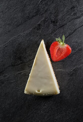 triangular cake with white cream on top and half juicy strawberries on a gray stone background